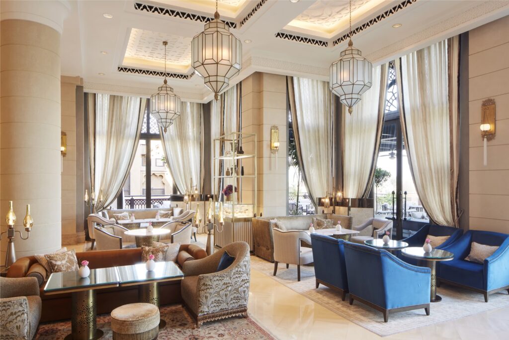 Elegant hotel lounge with ornate Moroccan-style lanterns, floor-to-ceiling curtains, and plush seating arranged around small tables
