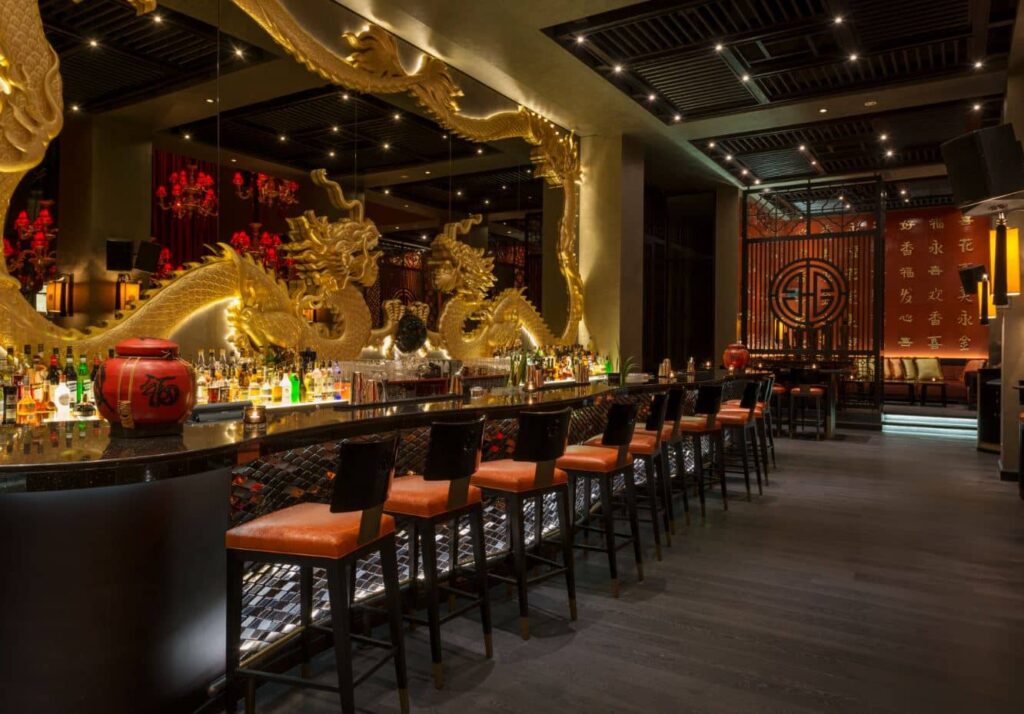 Buddha Bar Dubai with a long liquor-lined counter, red leather stools, and ornate golden dragon sculptures