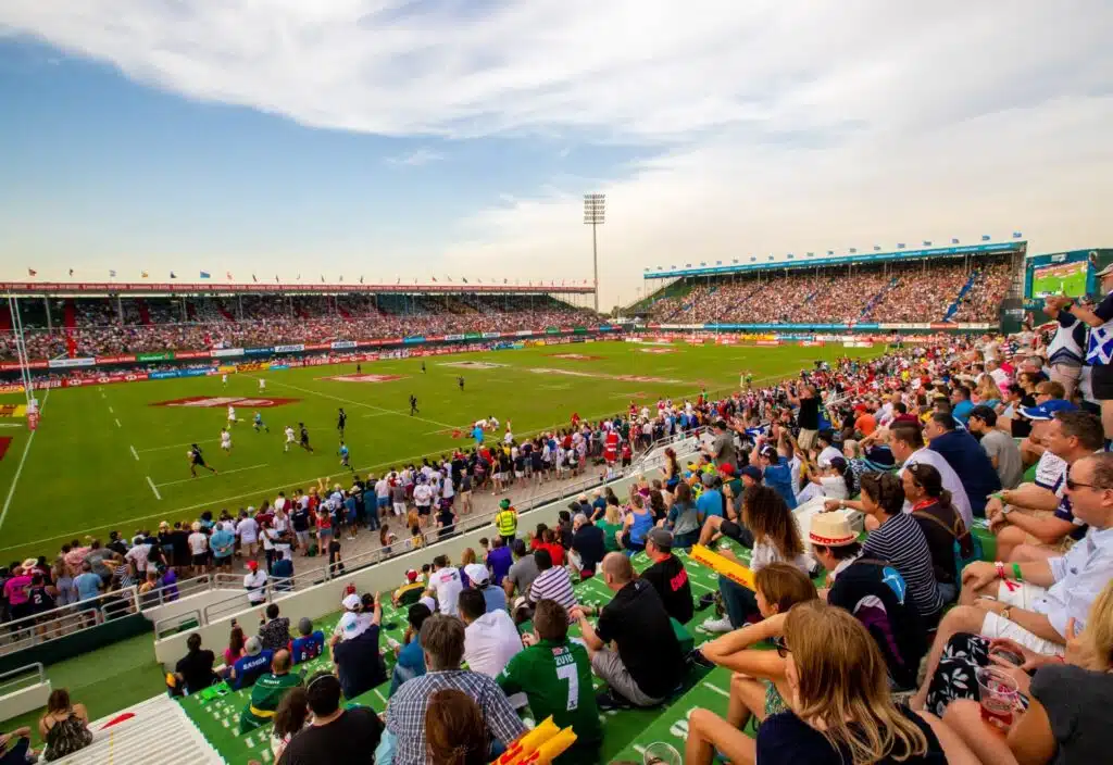 Crowded rugby stadium with players on the field and spectators filling the stands on a sunny day