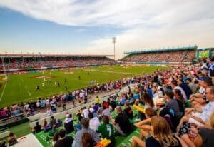 Crowded rugby stadium with players on the field and spectators filling the stands on a sunny day