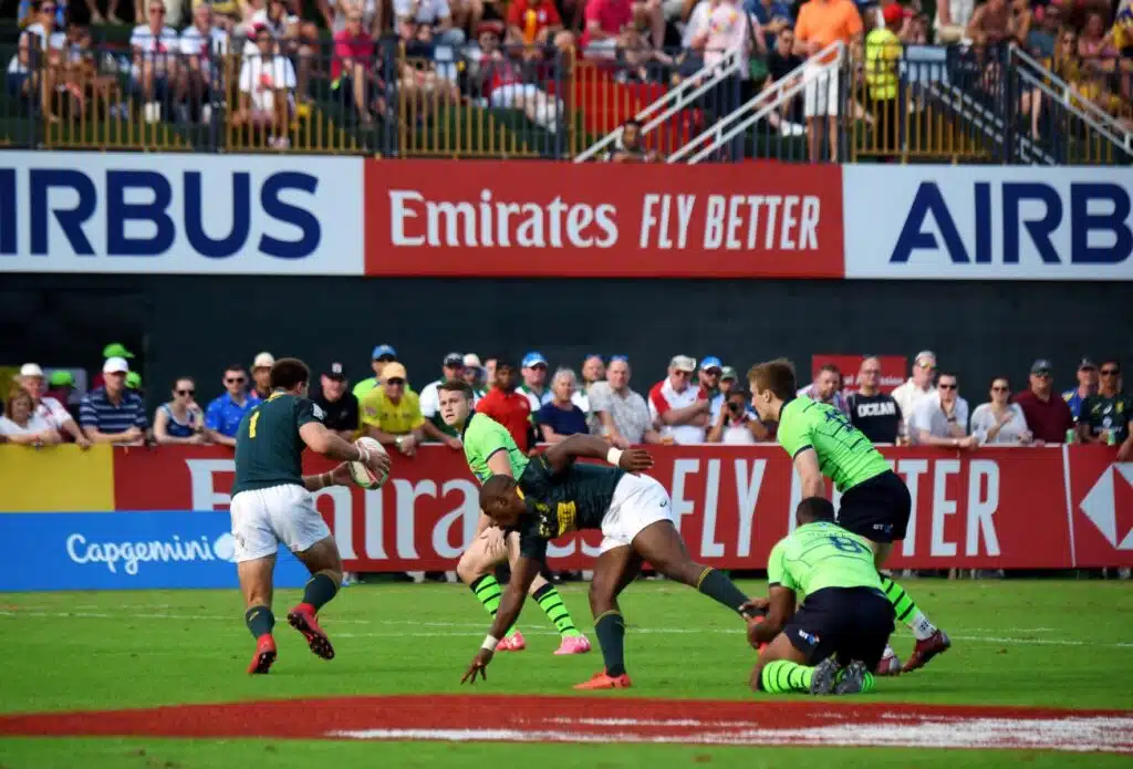 Rugby players tackle an opponent near the try line as spectators watch from behind advertising boards