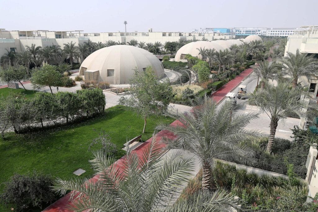Landscaped dubai sustainable city courtyard with palm trees, red pathways, modern white buildings, and several large dome-shaped structures