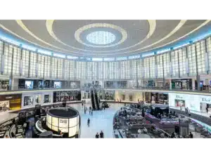Grand luxury shopping mall atrium with circular skylight, escalators, cafés, and designer stores including Fendi, Versace, and Dior