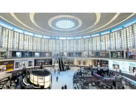Grand luxury shopping mall atrium with circular skylight, escalators, cafés, and designer stores including Fendi, Versace, and Dior