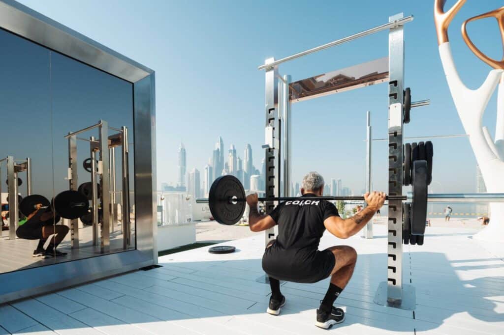 Coach squatting with a loaded barbell in an outdoor gym overlooking a city skyline