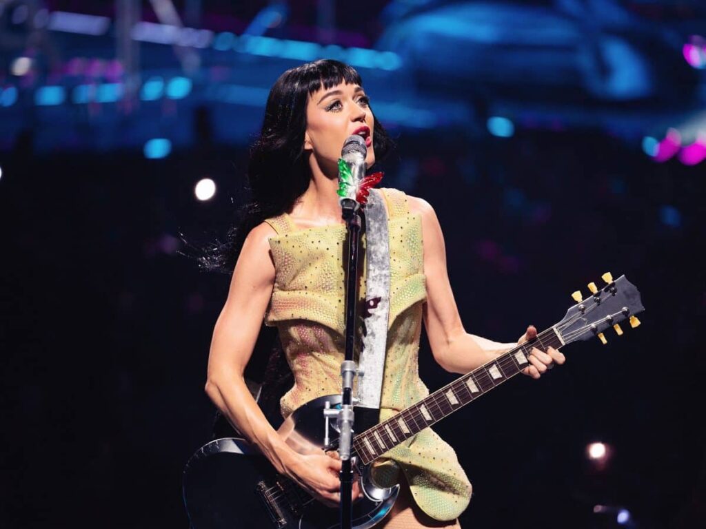 Katy Perry playing guitar and singing into a microphone during a concert