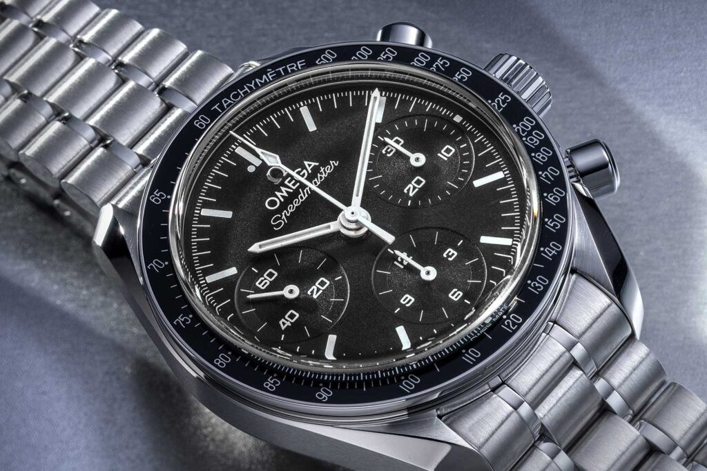 omega speedmaster 38mm chronograph watch with a black dial, silver bracelet, three subdials, and tachymeter bezel