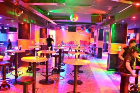 Colorfully lit nightclub with round tables, stools, a disco ball, and a small stage