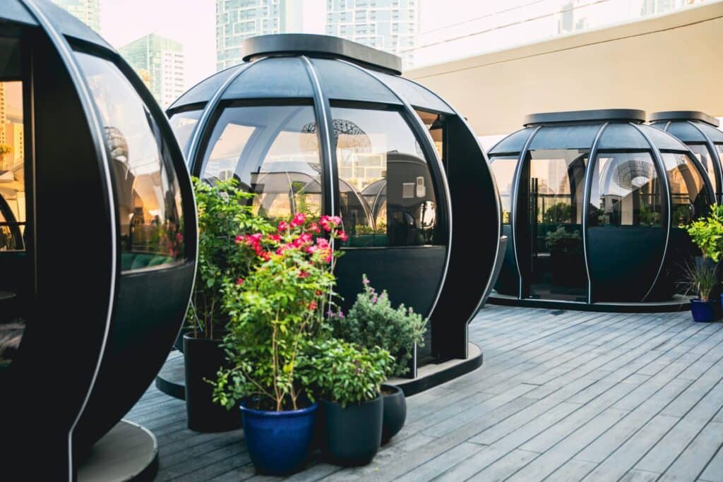 Transparent-domed dining pods with tables and chairs, surrounded by potted flowering plants on a rooftop terrace