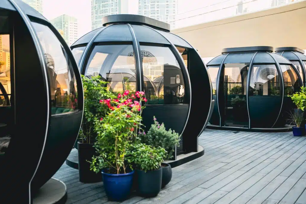 Transparent-domed dining pods with tables and chairs, surrounded by potted flowering plants on a rooftop terrace
