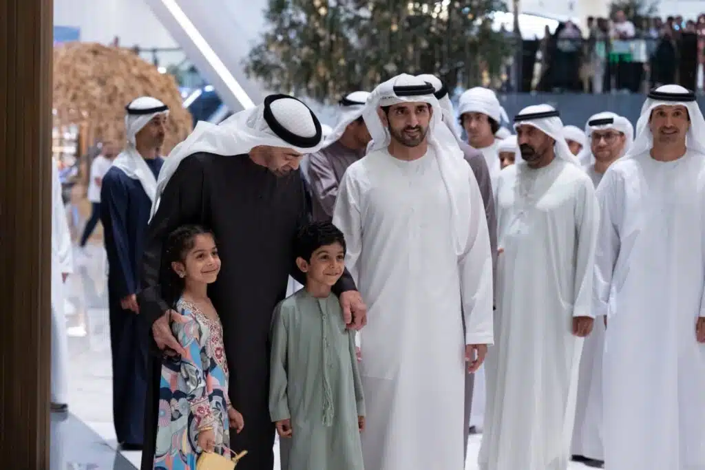 The President and Crown Prince and children gathered indoors, with a man in black embracing two children among men in traditional white attire for a UAE viral moment.