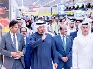 A large group of officials and shoppers gathers inside a busy supermarket, led by men in traditional Gulf attire