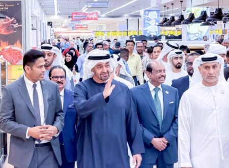 A large group of officials and shoppers gathers inside a busy supermarket, led by men in traditional Gulf attire