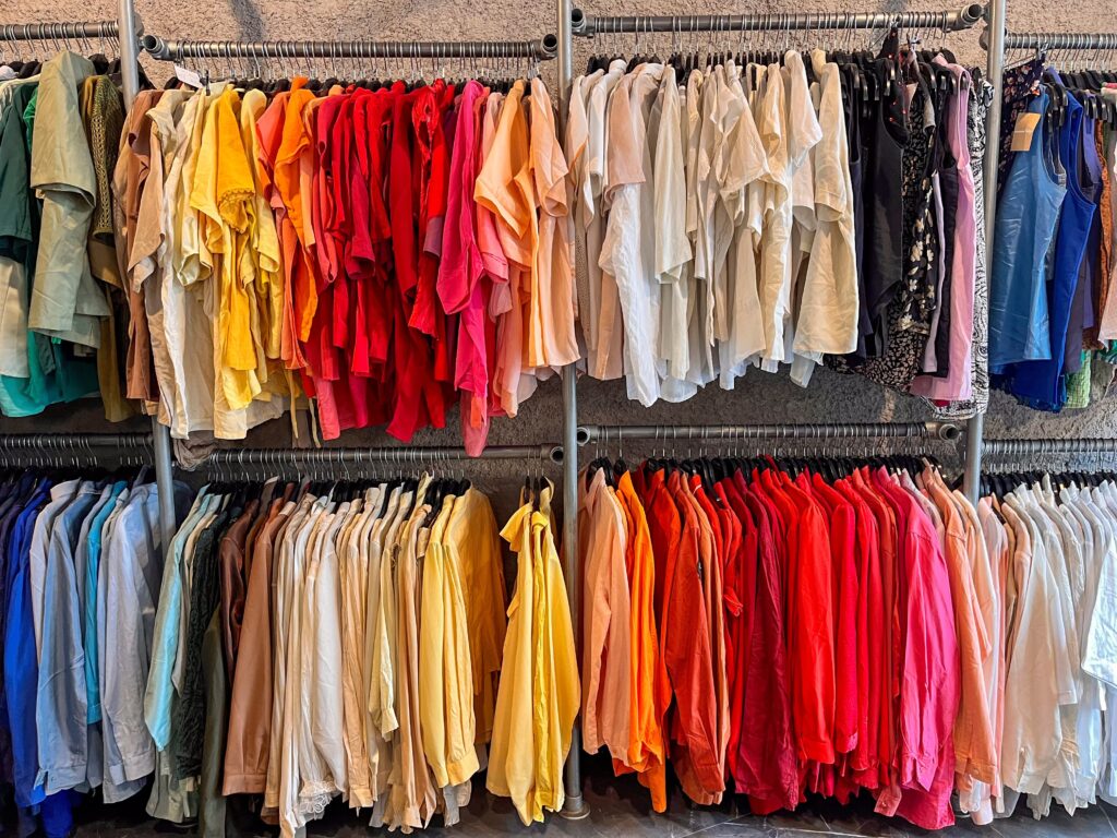 Clothing racks filled with garments arranged by color, from blue and neutral tones to yellow, orange, red, pink, and black
