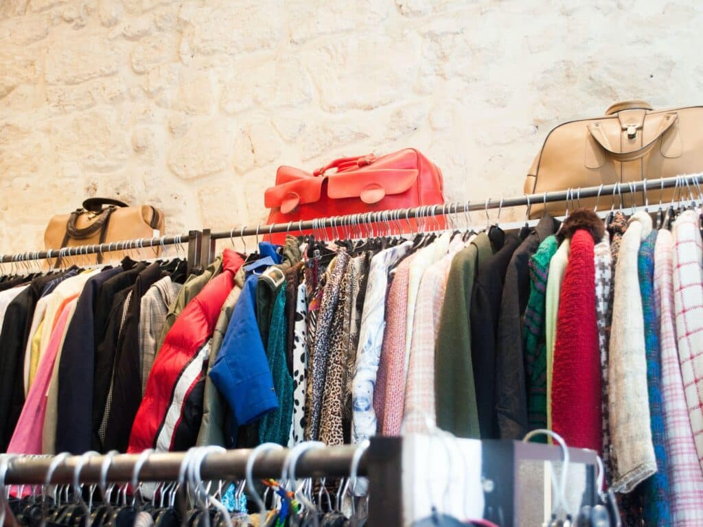 Thrift Clothing racks filled with colorful garments beneath handbags in a boutique
