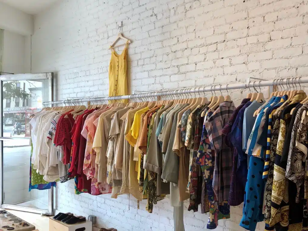 Clothing racks display a colorful assortment of vintage-style garments in a boutique with white brick walls