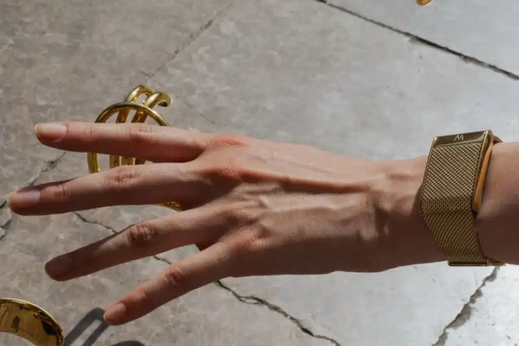 Hand wearing a gold mesh WHOOP Meridian and multiple gold rings