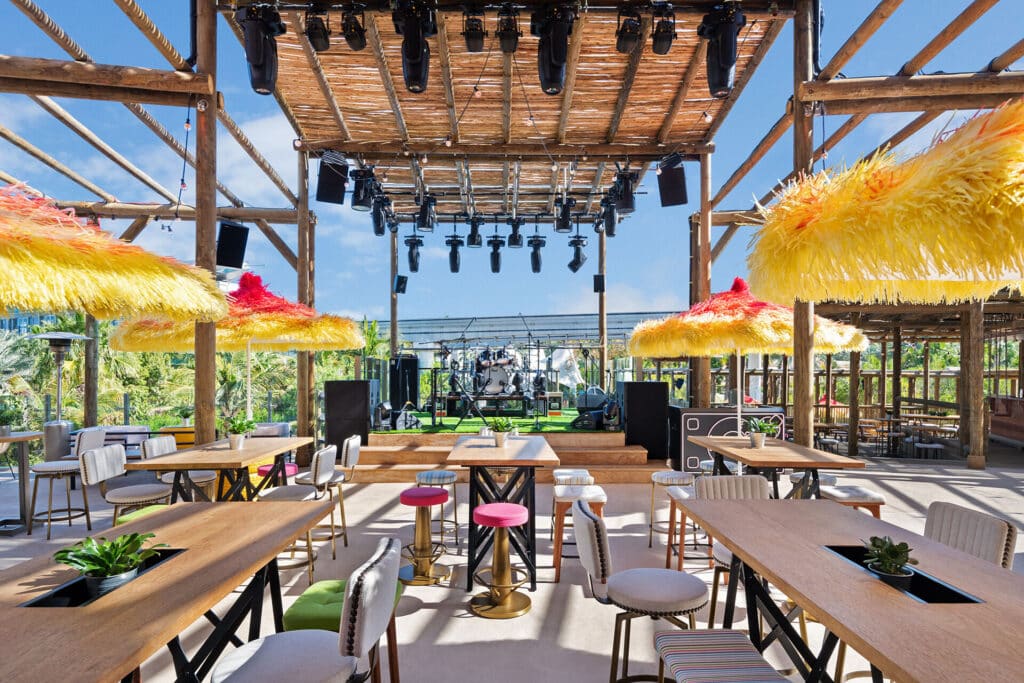 Wavehouse Dubai with colorful umbrellas, tables and chairs, and a live music stage beneath a wooden pergola