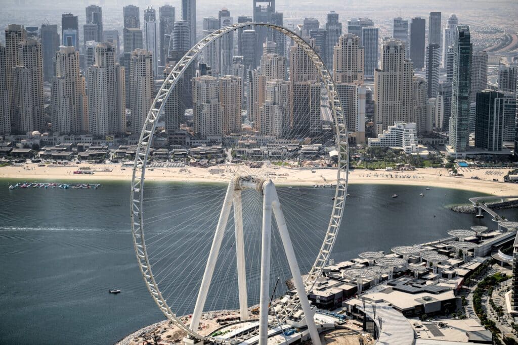 Aerial view of Ain Dubai Ferris wheel beside a waterfront beach and dense Dubai skyline