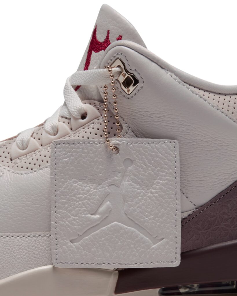 Close-up of a white and burgundy basketball shoe featuring a stitched Jumpman logo and gold ball-chain tag