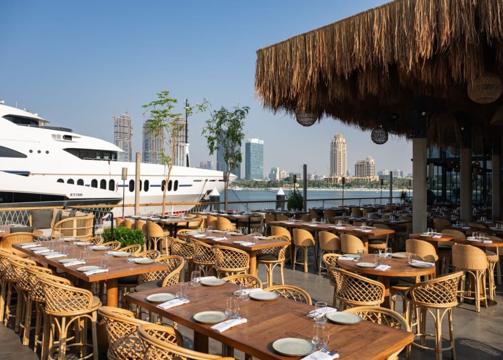 Bar du Port Dubai Waterfront restaurant terrace with set tables, a large white yacht, and a modern city skyline across the water