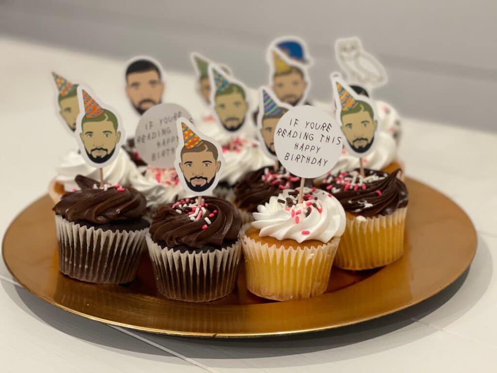 Birthday cupcakes decorated with cartoon portraits wearing party hats and signs reading “If you’re reading this, happy birthday.”