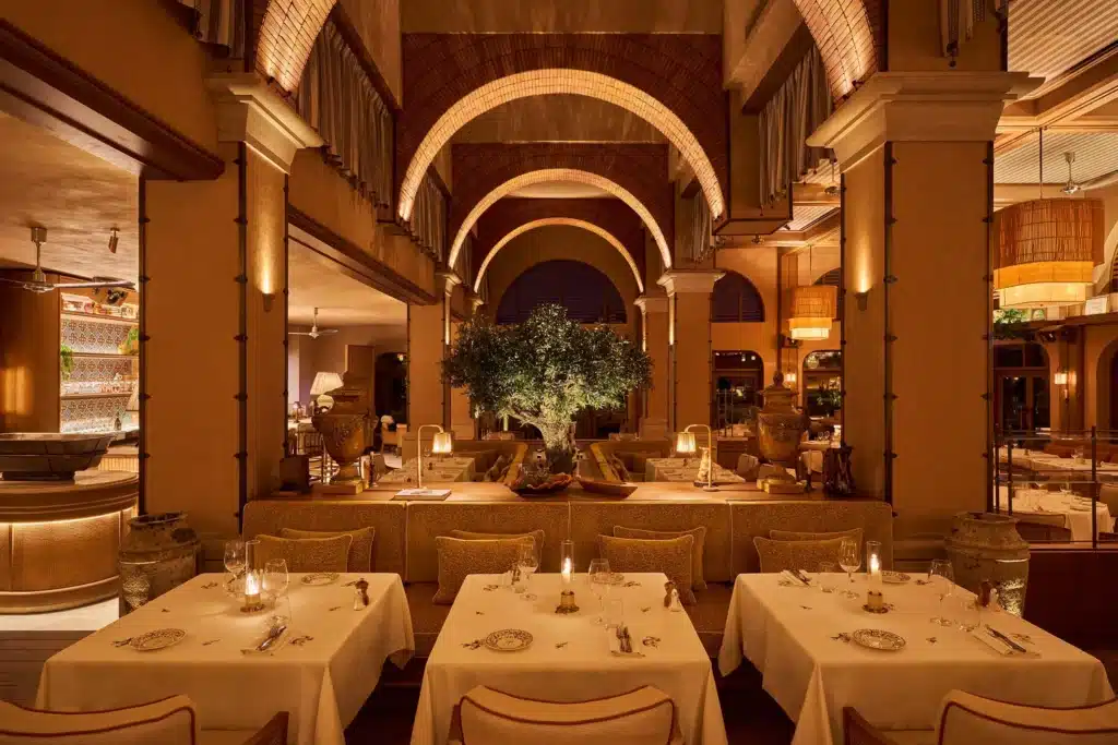 Elegant Gigi Rigolatto Dubai restaurant dining room with white-tablecloth tables, arched brick ceilings, warm lighting, and a central olive tree