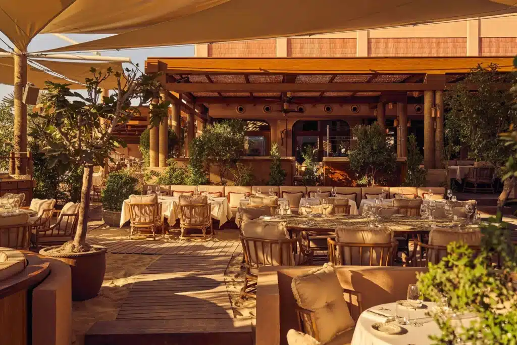 Gigi Rigolatto Dubai outdoor restaurant patio with elegantly set tables, cushioned wicker chairs, greenery, and wooden shade structures