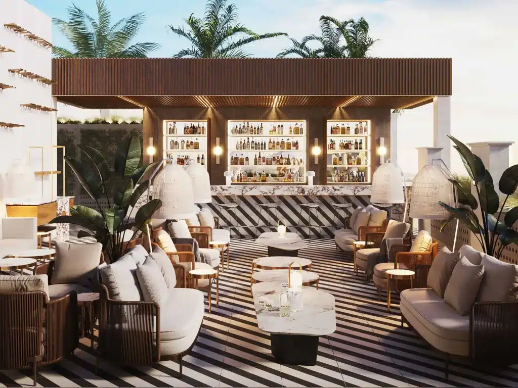 Rooftop bar with illuminated liquor shelves, striped flooring, lounge seating, tropical plants, and palm trees