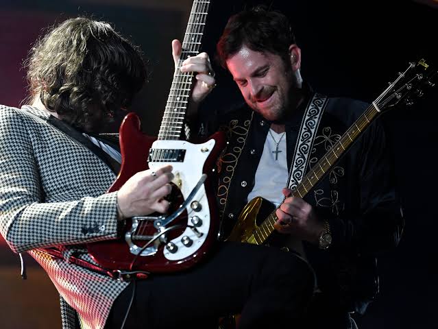 Kings of Leon perform side by side onstage, playing electric guitars