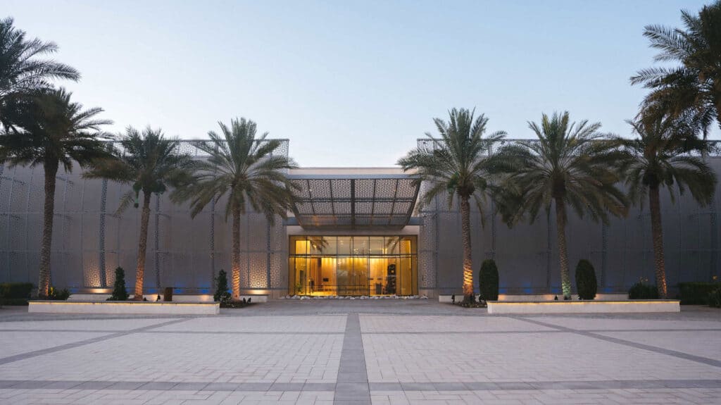 Manarat Al Saadiyat entrance framed by palm trees, with illuminated geometric screens and a broad tiled plaza