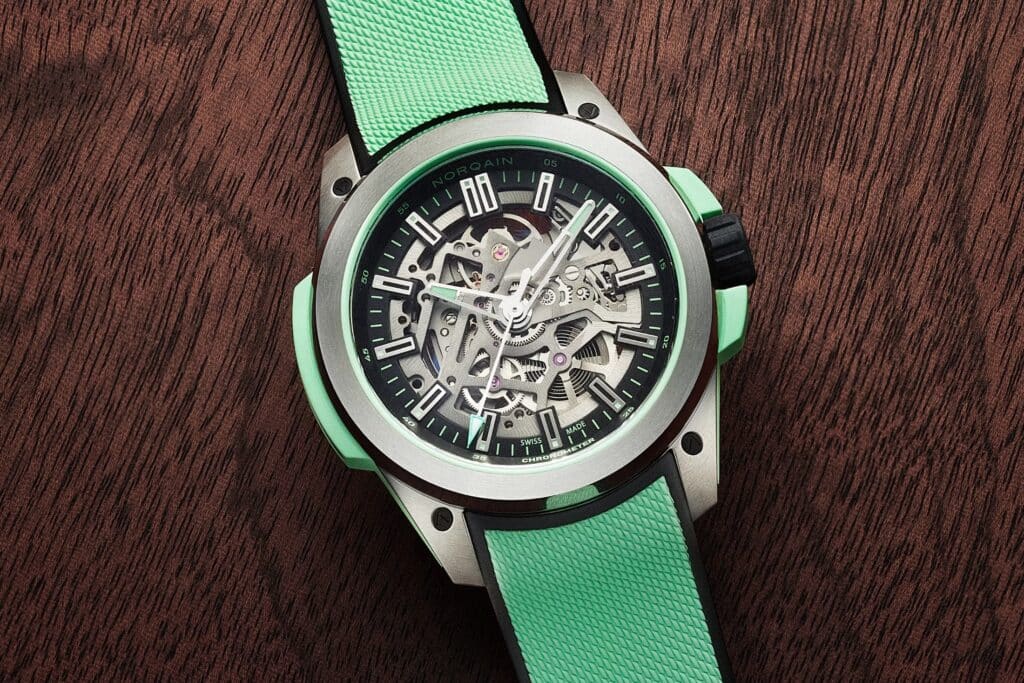 Close-up of a green Norqain skeletonized wristwatch with a textured strap on a wooden surface