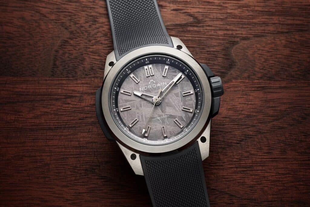 NORQAIN Wild ONE with a grey patterned meteorite dial, metallic top plate and textured grey strap on wood.