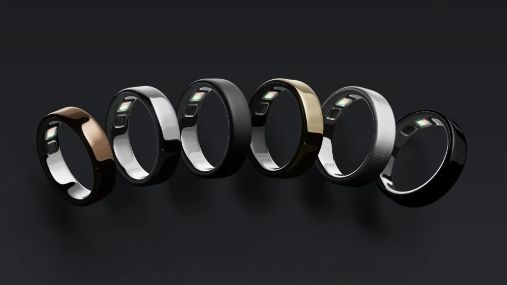 Six glossy ŌURA Ring fitness-tracking rings in black, silver, gold, and bronze, with visible sensor interiors