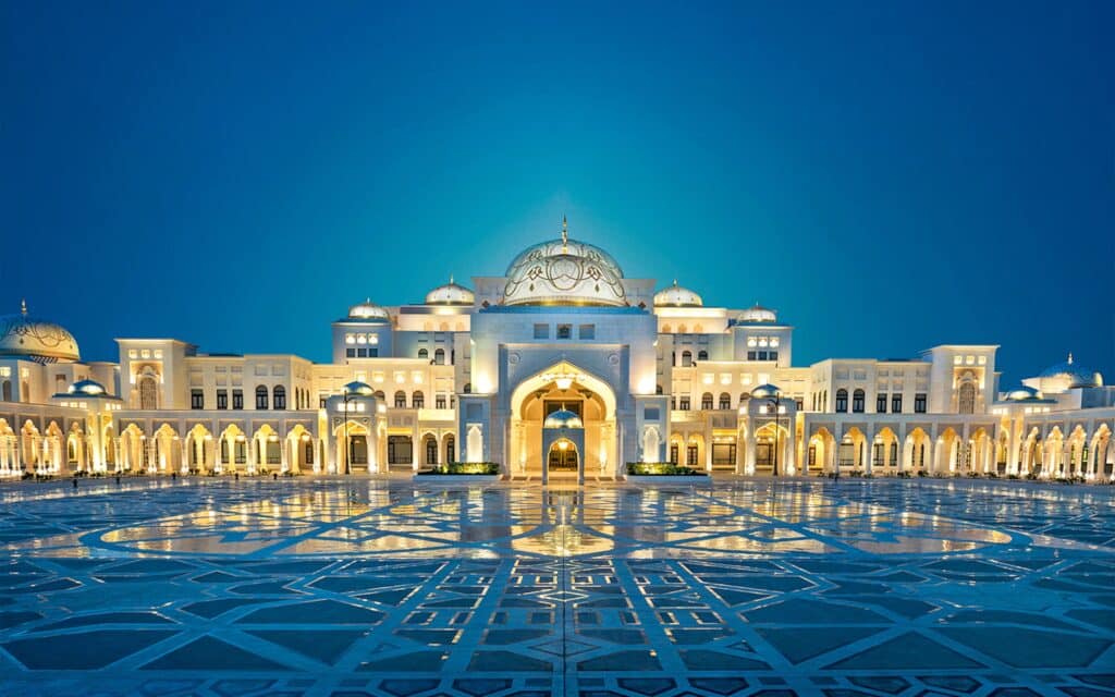 Illuminated grand Islamic-style palace with domes and arches, reflected in a geometric courtyard at dusk