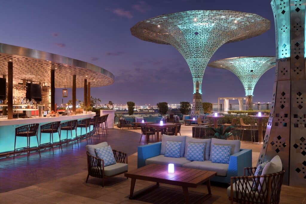 Rosewood Abu Dhabi Rooftop bar and lounge at dusk, with glowing geometric mushroom-shaped canopies, outdoor seating, and a city skyline