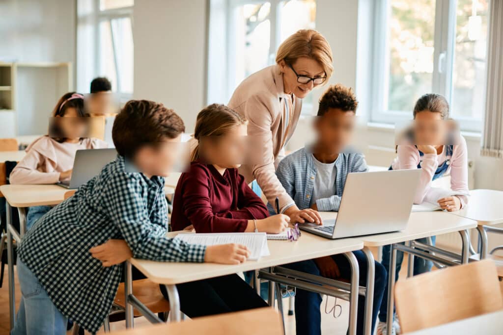 New School Photography Privacy rules explained: Teacher assisting students working together in a classroom with laptops and notebooks