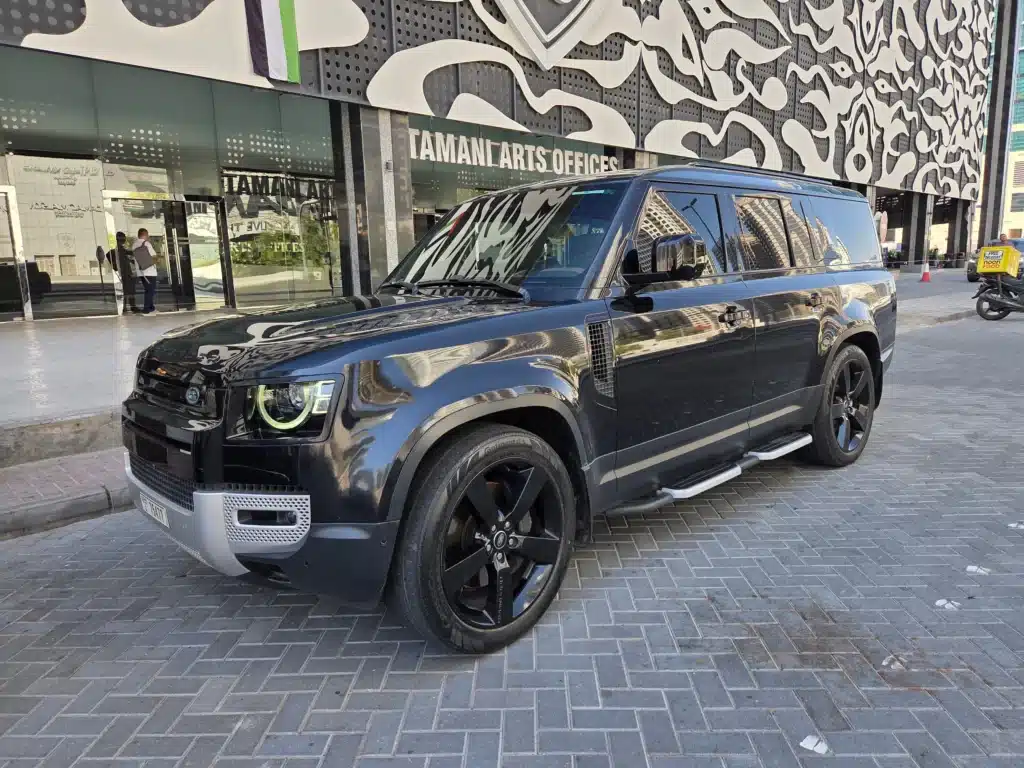Black Land Rover Defender car parked outside the Taman I Arts Offices in Dubai , beneath a large Arabic calligraphy mural