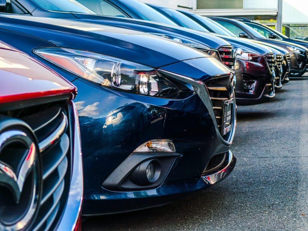 Row of cars parked at a dealership, viewed close up from the front