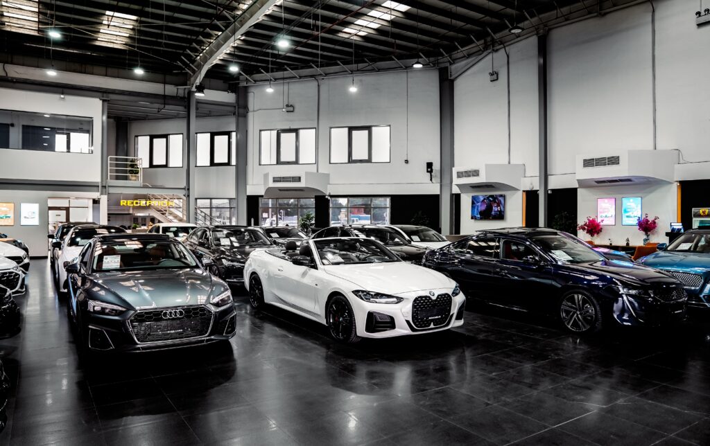 Luxury car dealership showroom displaying rows of cars, with a reception desk and “RECEPTION” sign