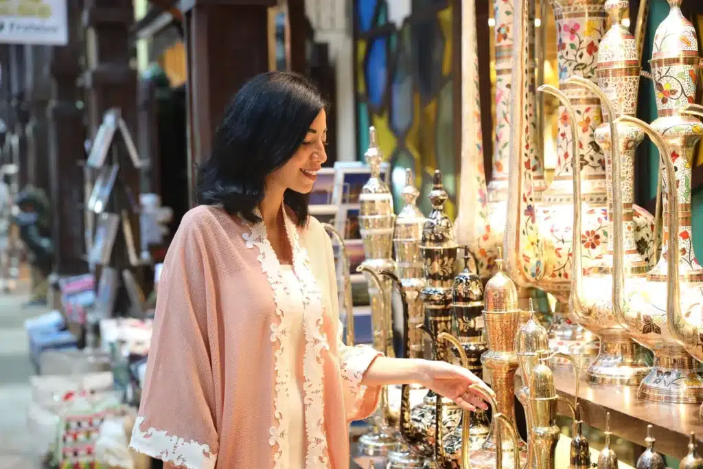 Woman browsing ornate metal and ceramic vessels in a colorful Souk Madinat Jumeirah market shop