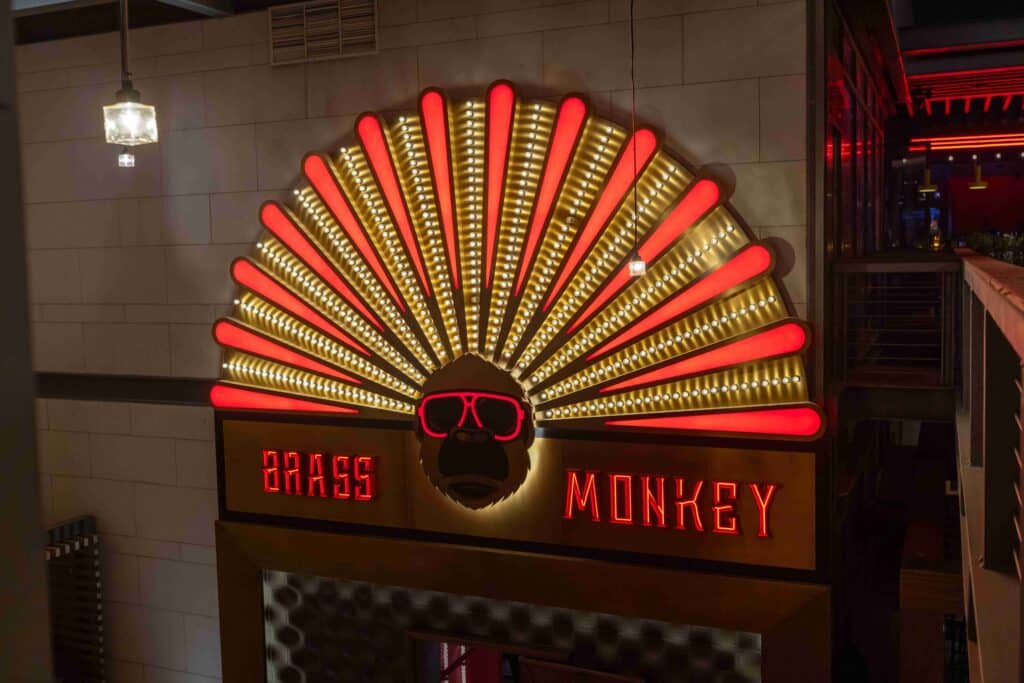 Neon sign for Brass Monkey featuring a stylized monkey wearing sunglasses beneath a red-and-gold fan of lights