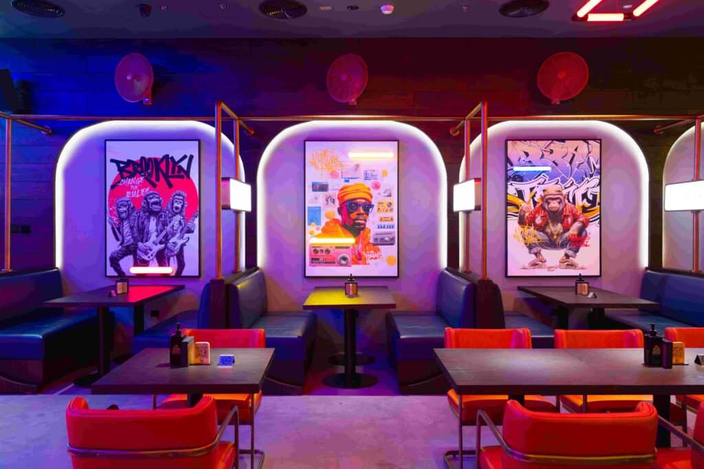 Neon-lit brass monkey city walk restaurant interior with booths, tables, and three colorful music-themed posters on the wall